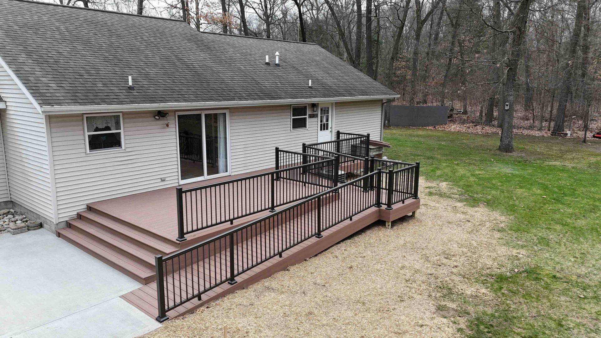 Back porch with wooden accessibility ramp and railings beside a white house, overlooking a gravel yard.