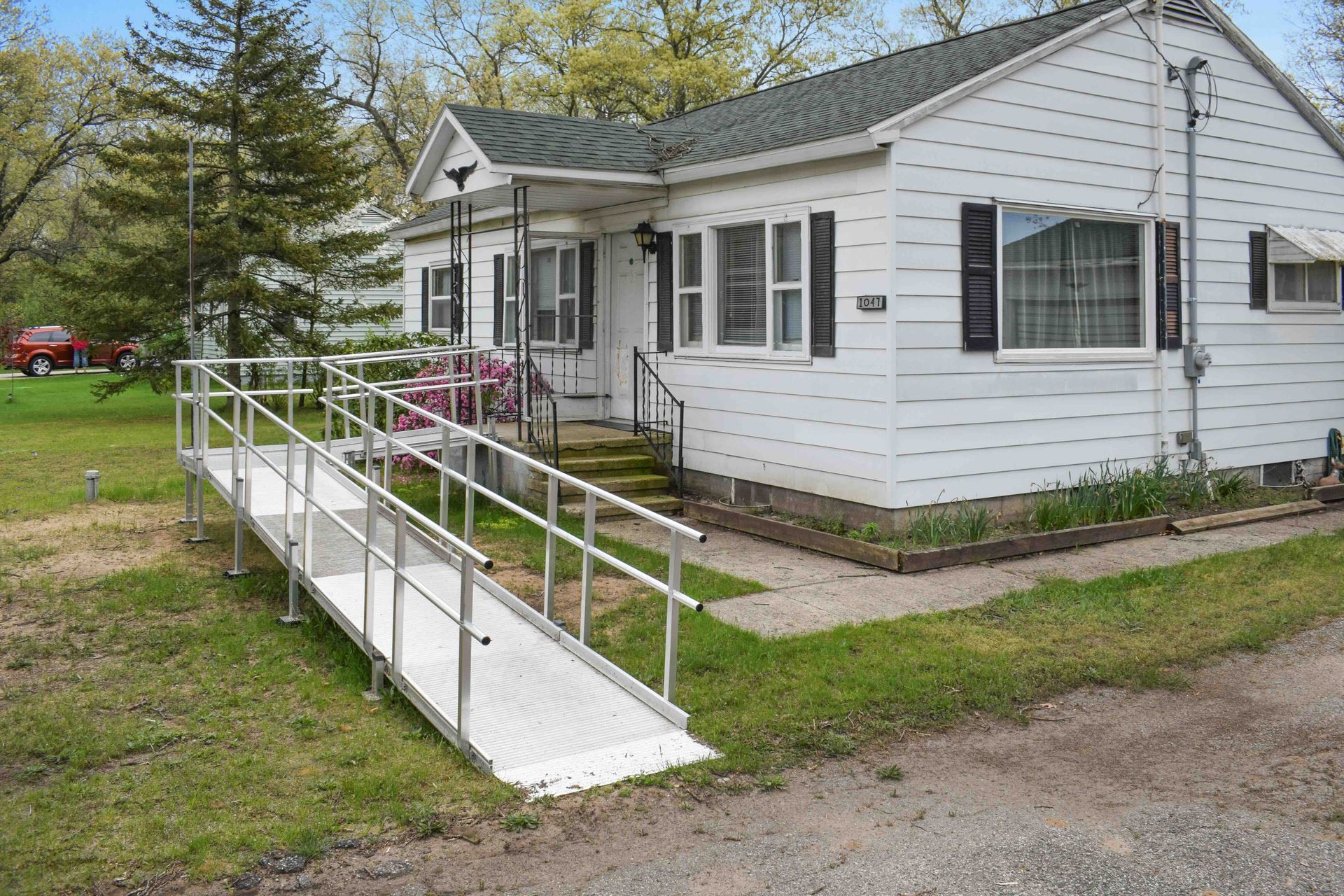White house with a wheelchair ramp and flower beds in a grassy yard