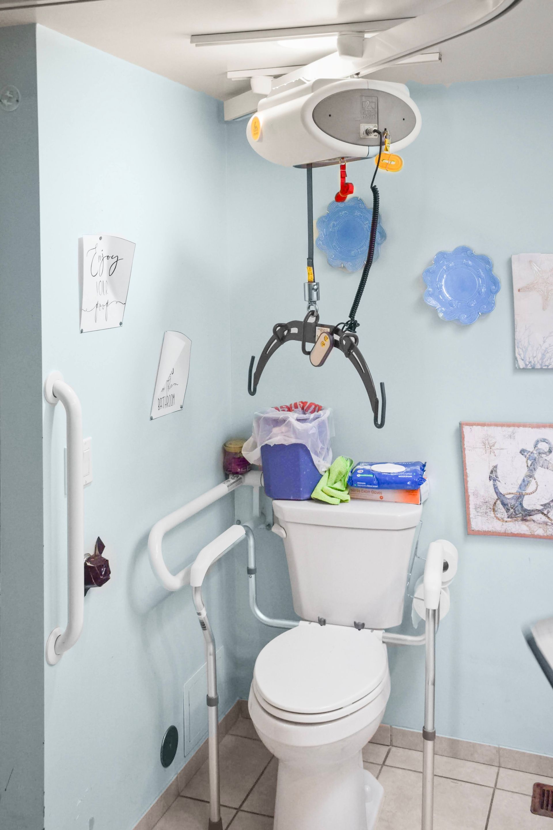 Accessible bathroom with toilet lift, grab bars, and transfer sling under an overhead hoist