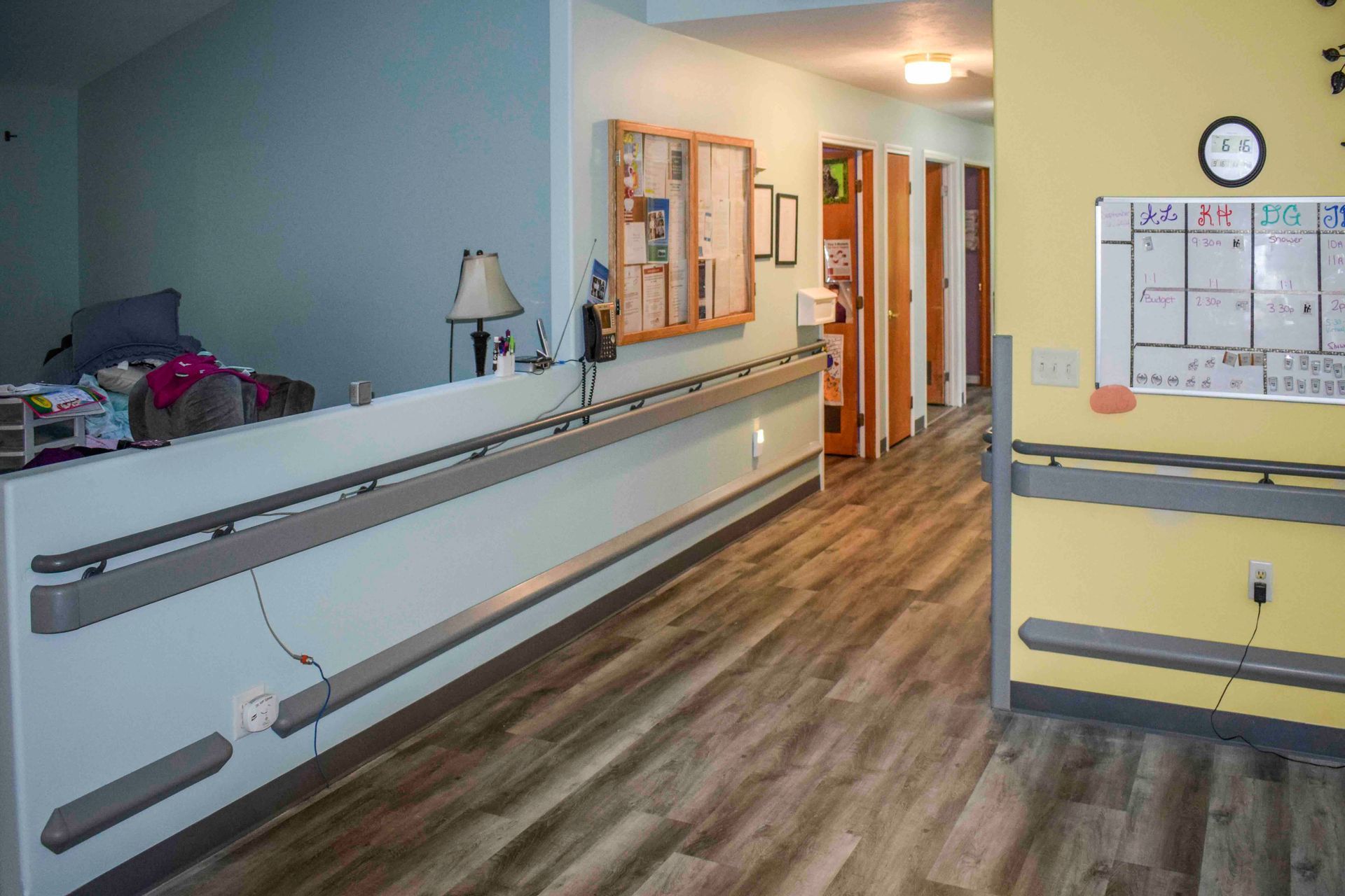 Hallway with gray handrails, light blue and yellow walls, wooden doors, and wooden-look flooring.