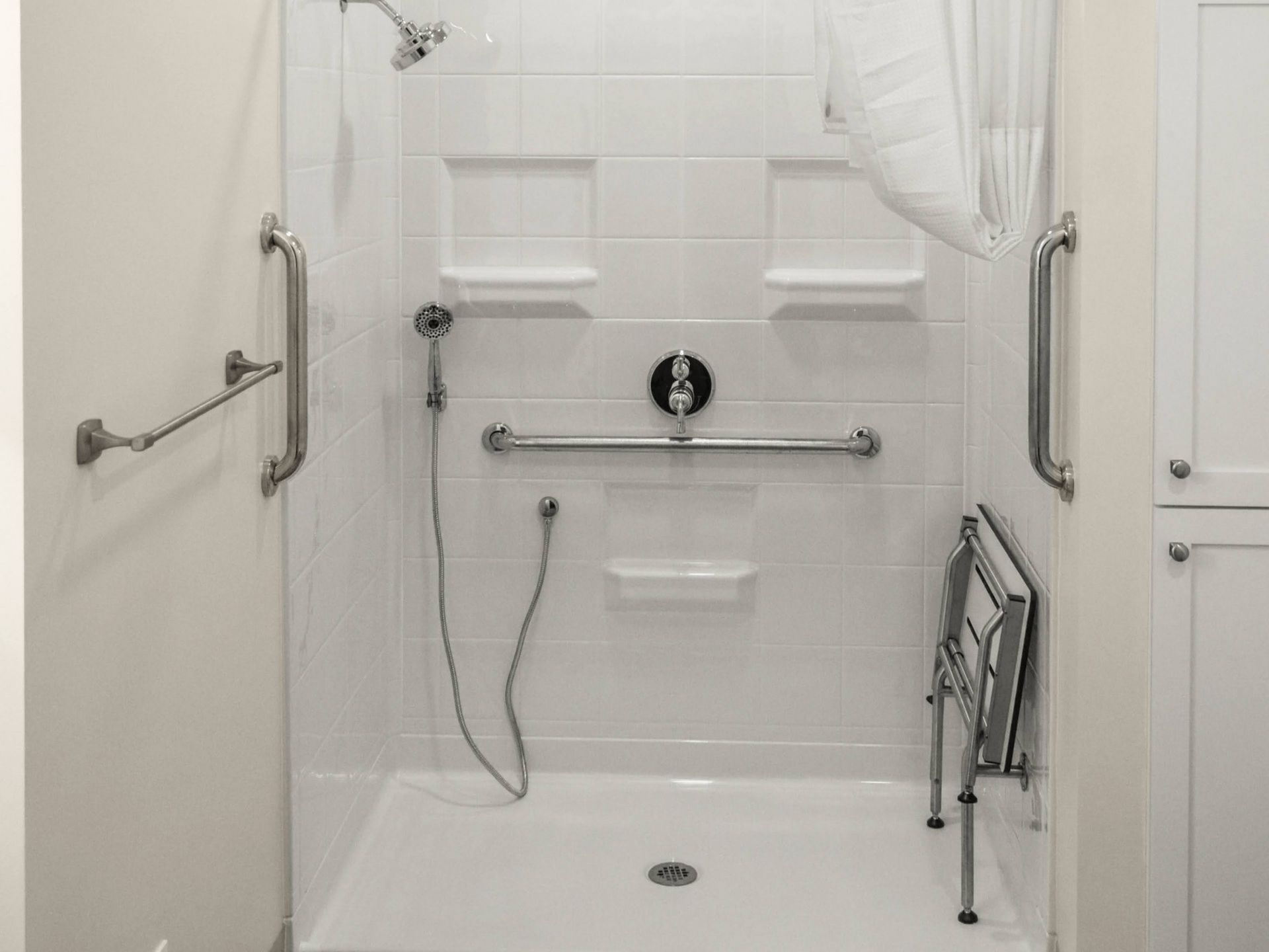 Accessible white shower stall with grab bars and a fold-down shower seat