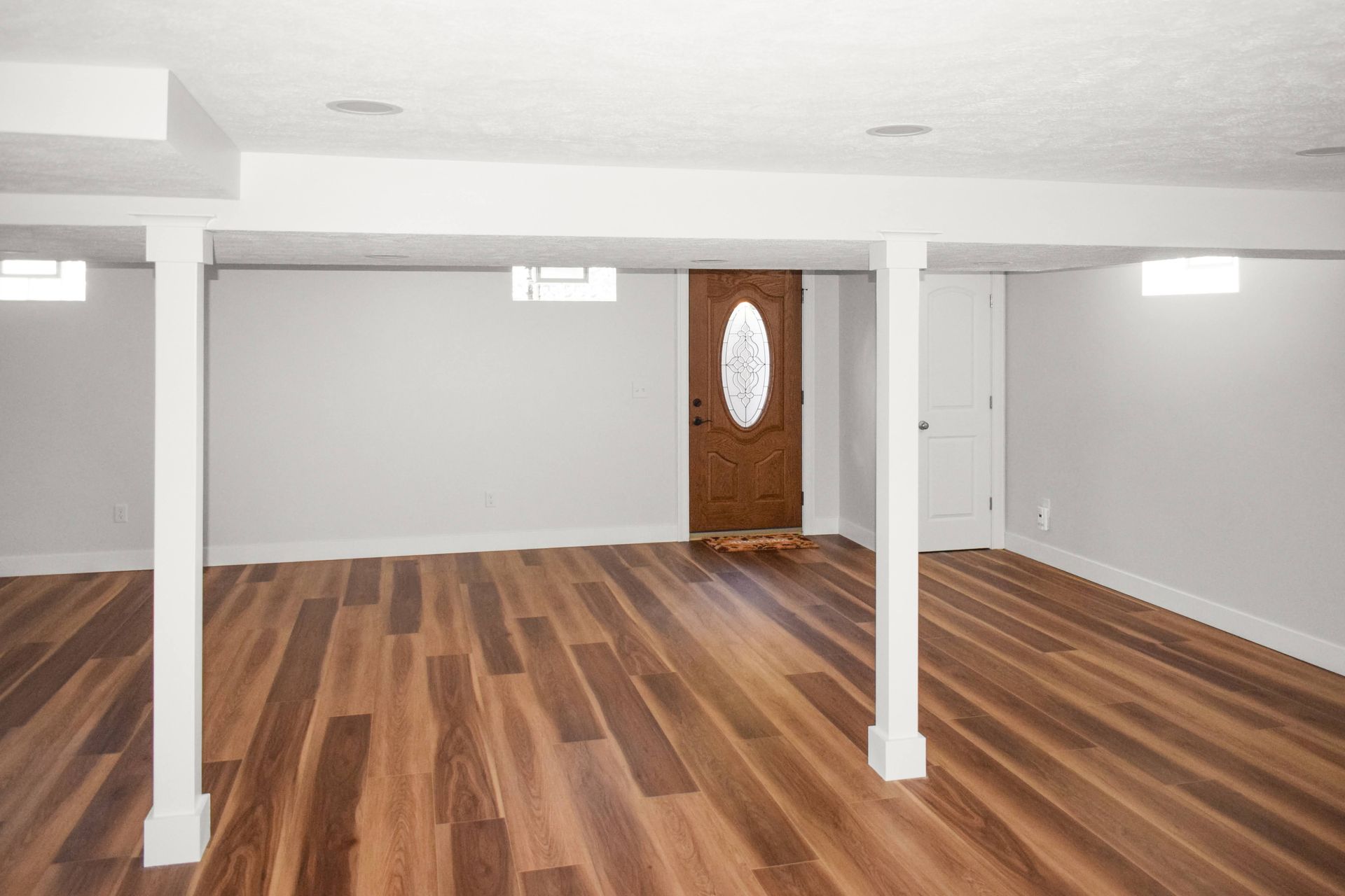 An empty basement with hardwood floors and white walls.