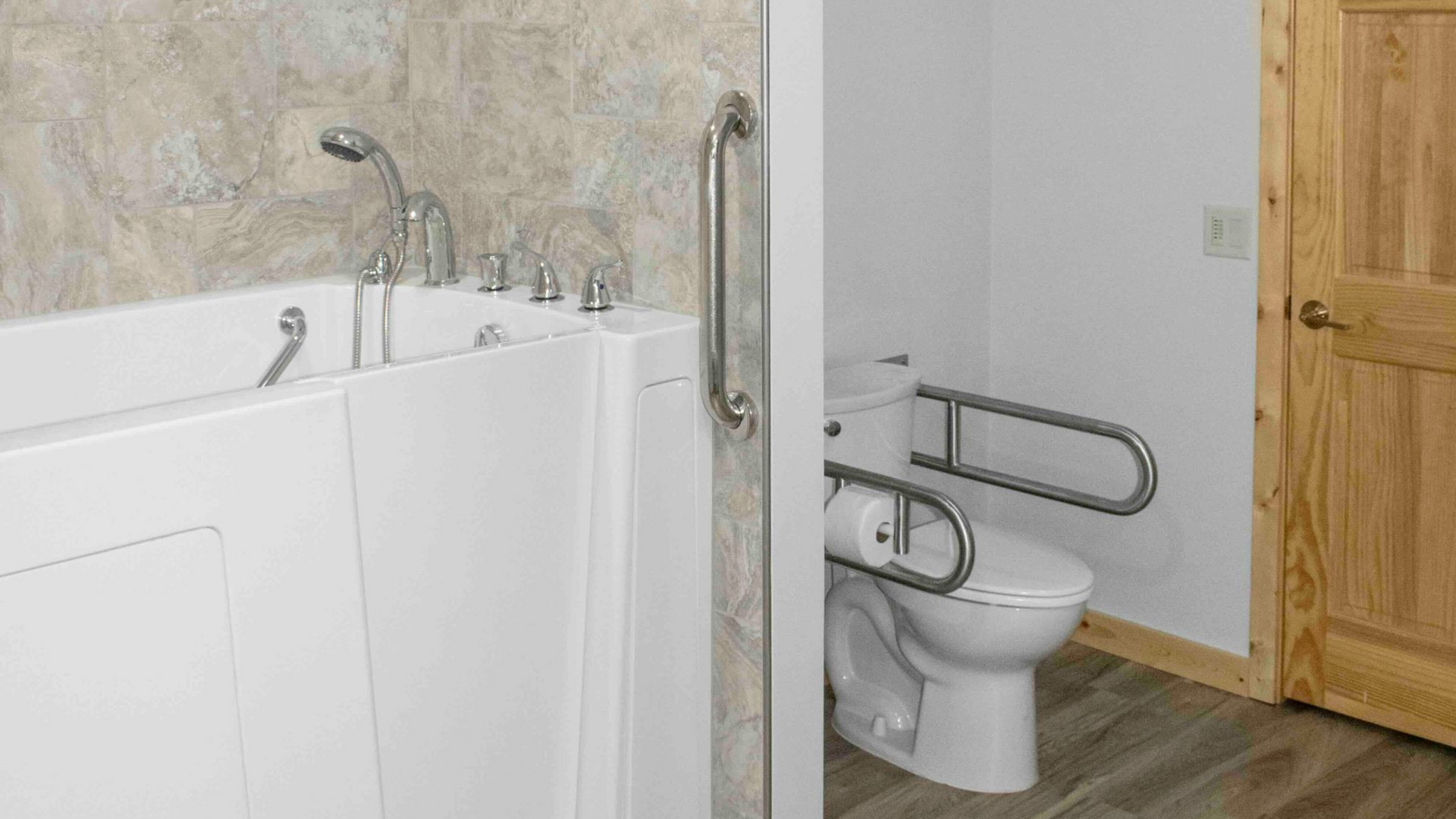 An accessible bathroom featuring a white walk-in bathtub with a grab bar and a toilet equipped with folding support rails.