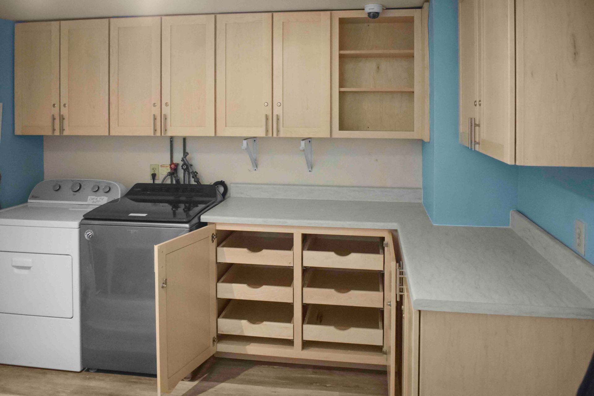 Small kitchen with beige cabinets, blue walls, white stove, and open lower cabinet showing empty pull-out shelves