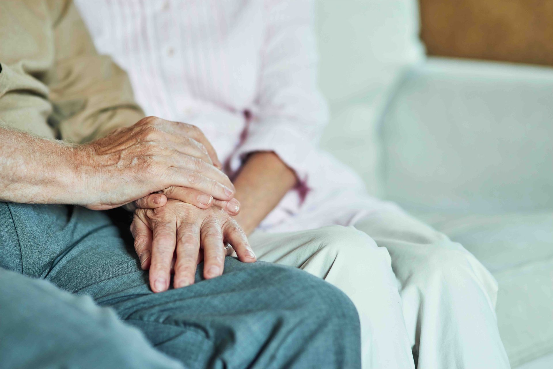 An elderly couple is sitting on a couch holding hands.