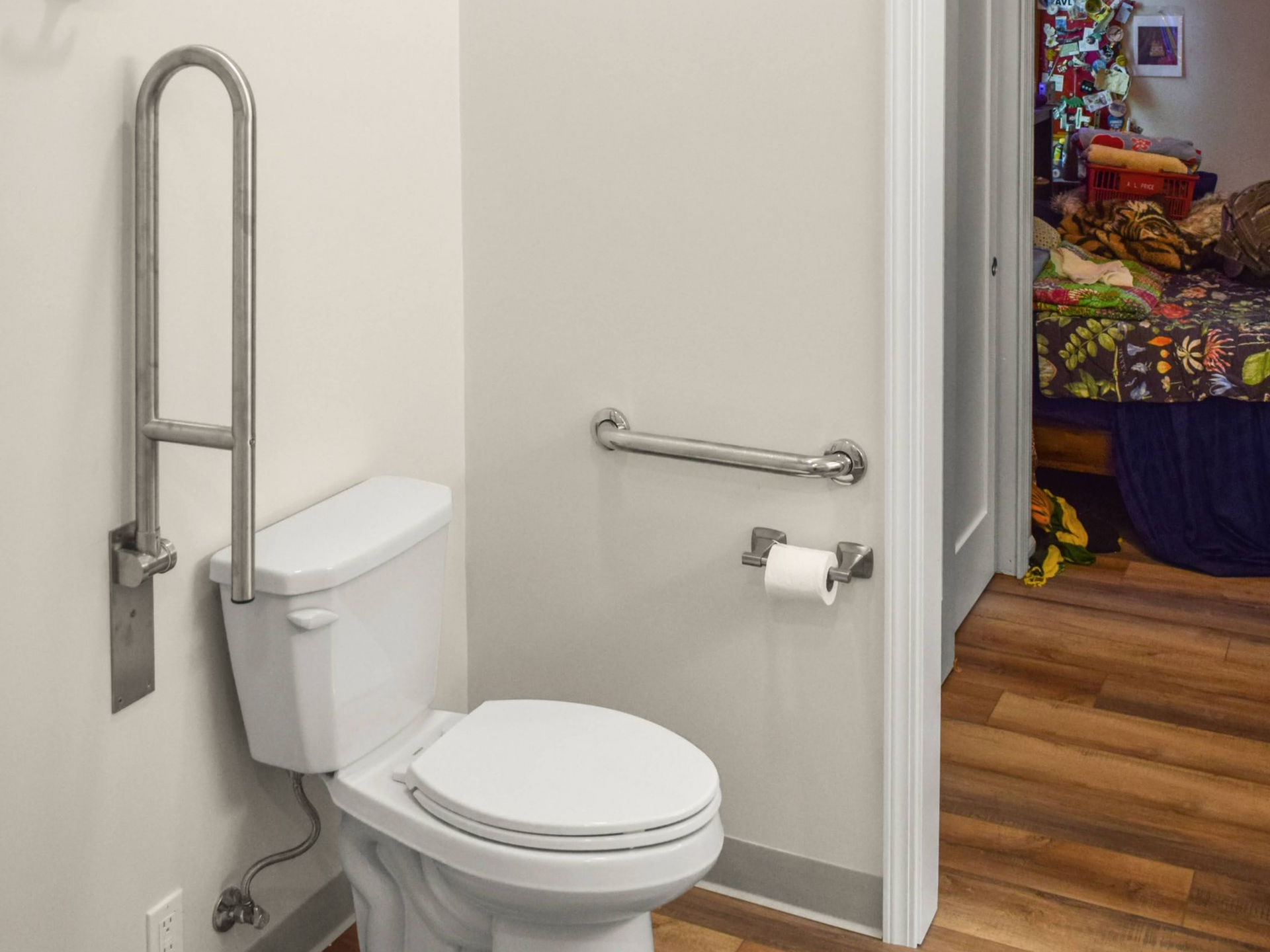 Accessible bathroom with toilet, grab bars, and open doorway to another room.