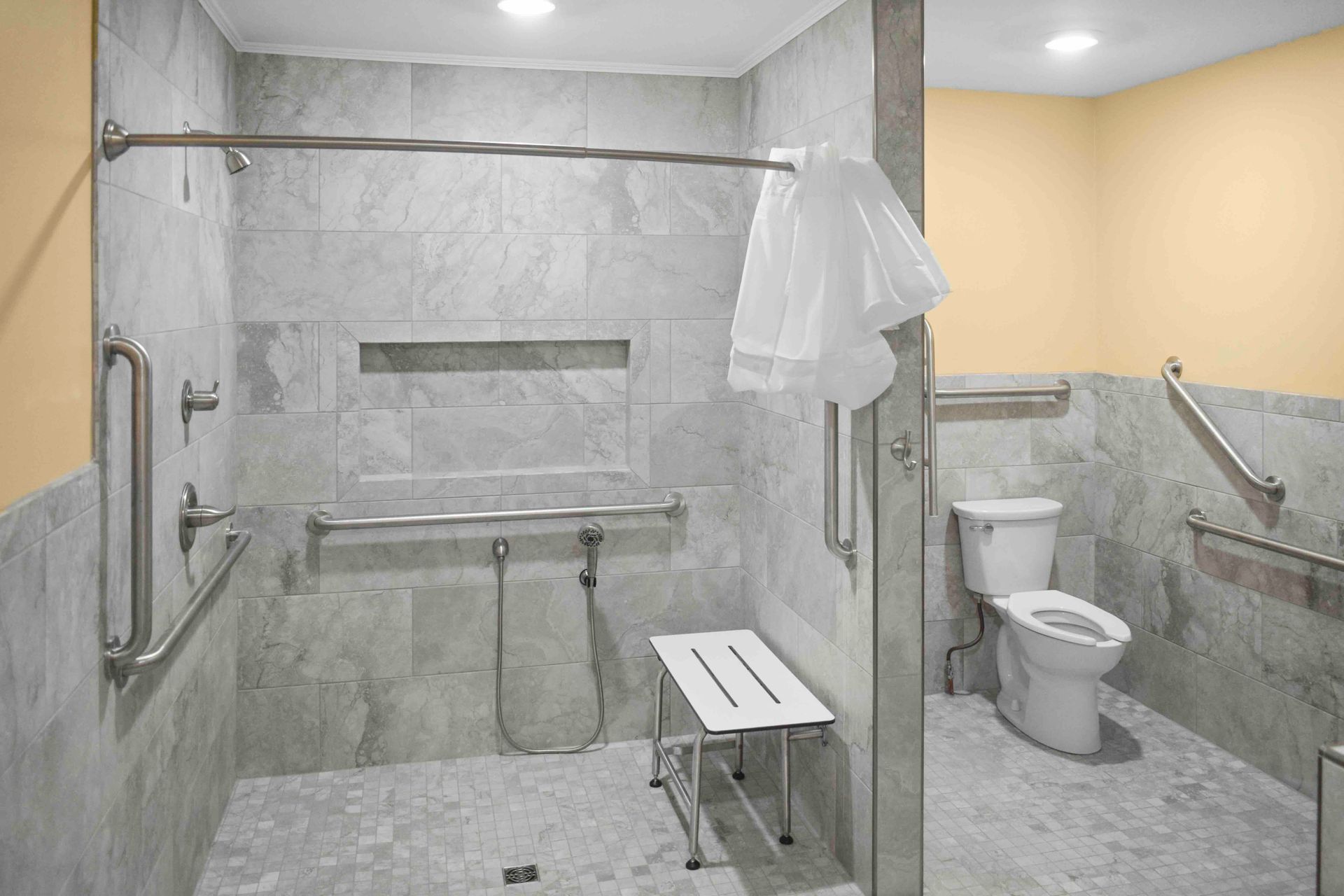 Accessible bathroom with gray tile, shower bench, grab bars, toilet, and shower curtain.