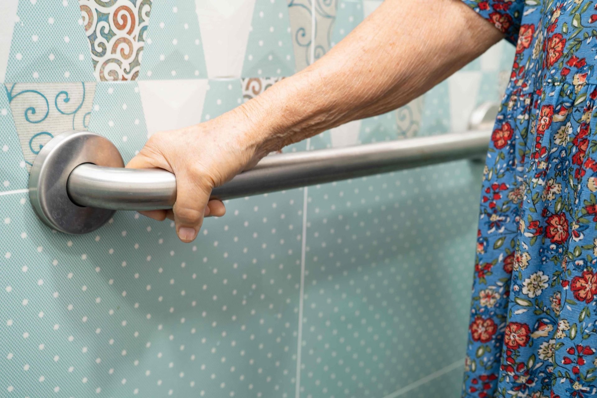 Hand gripping a stainless steel bathroom grab bar beside a tiled wall