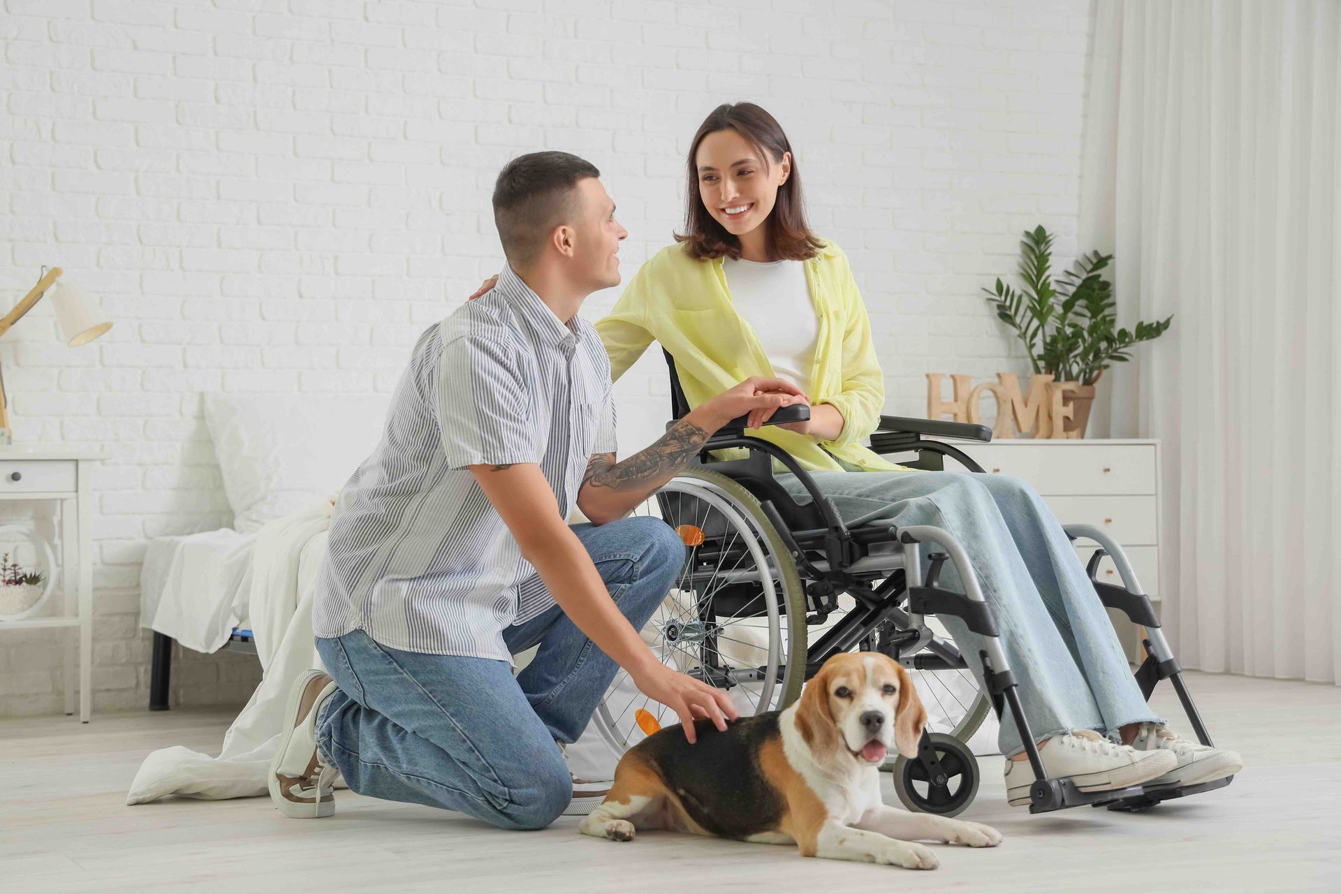 A man is kneeling next to a woman in a wheelchair and a dog.