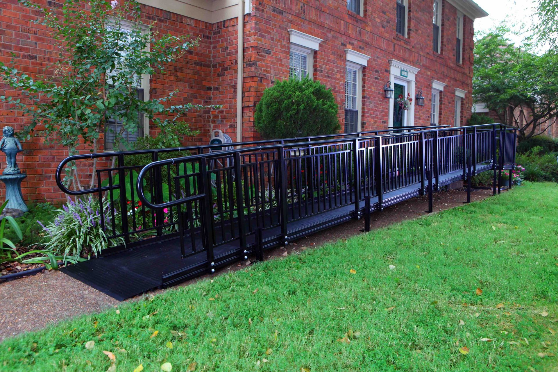 Black accessibility ramp with railings beside a red brick building and green lawn