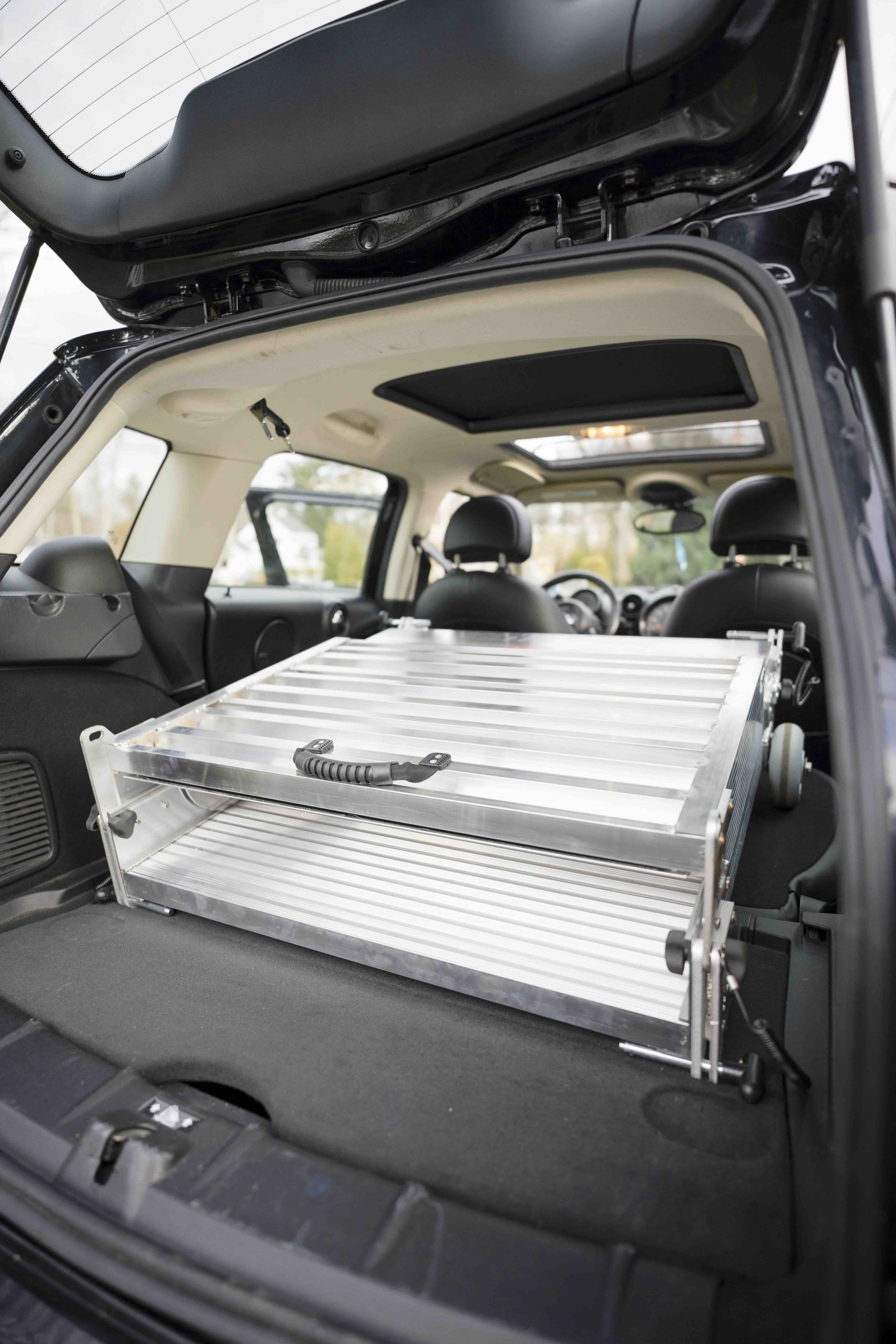 SUV cargo area with a silver metal folding portable wheelchair ramp secured inside, rear hatch open