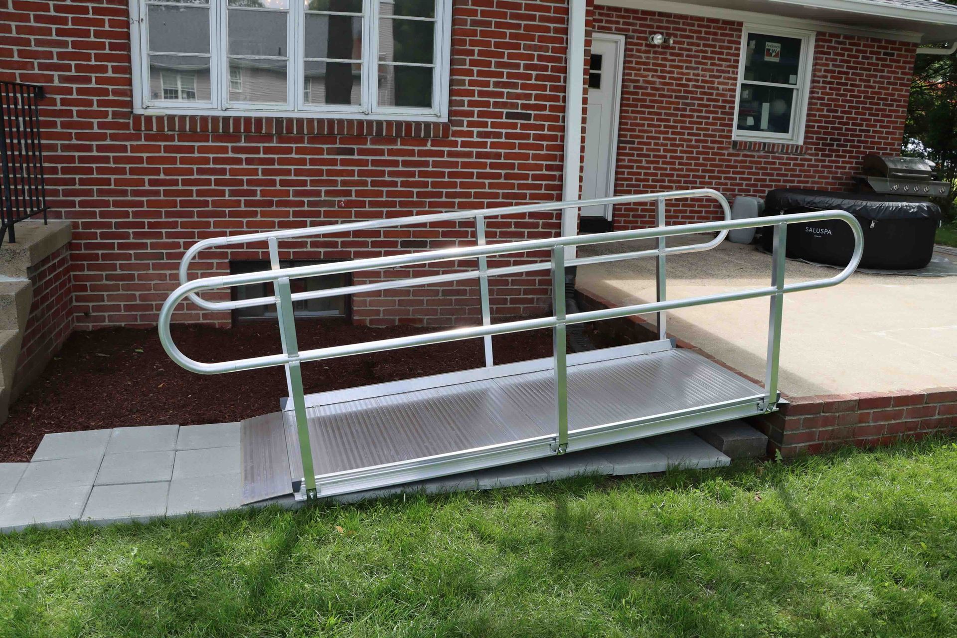 Portable wheelchair ramp on grass beside a brick building entrance.