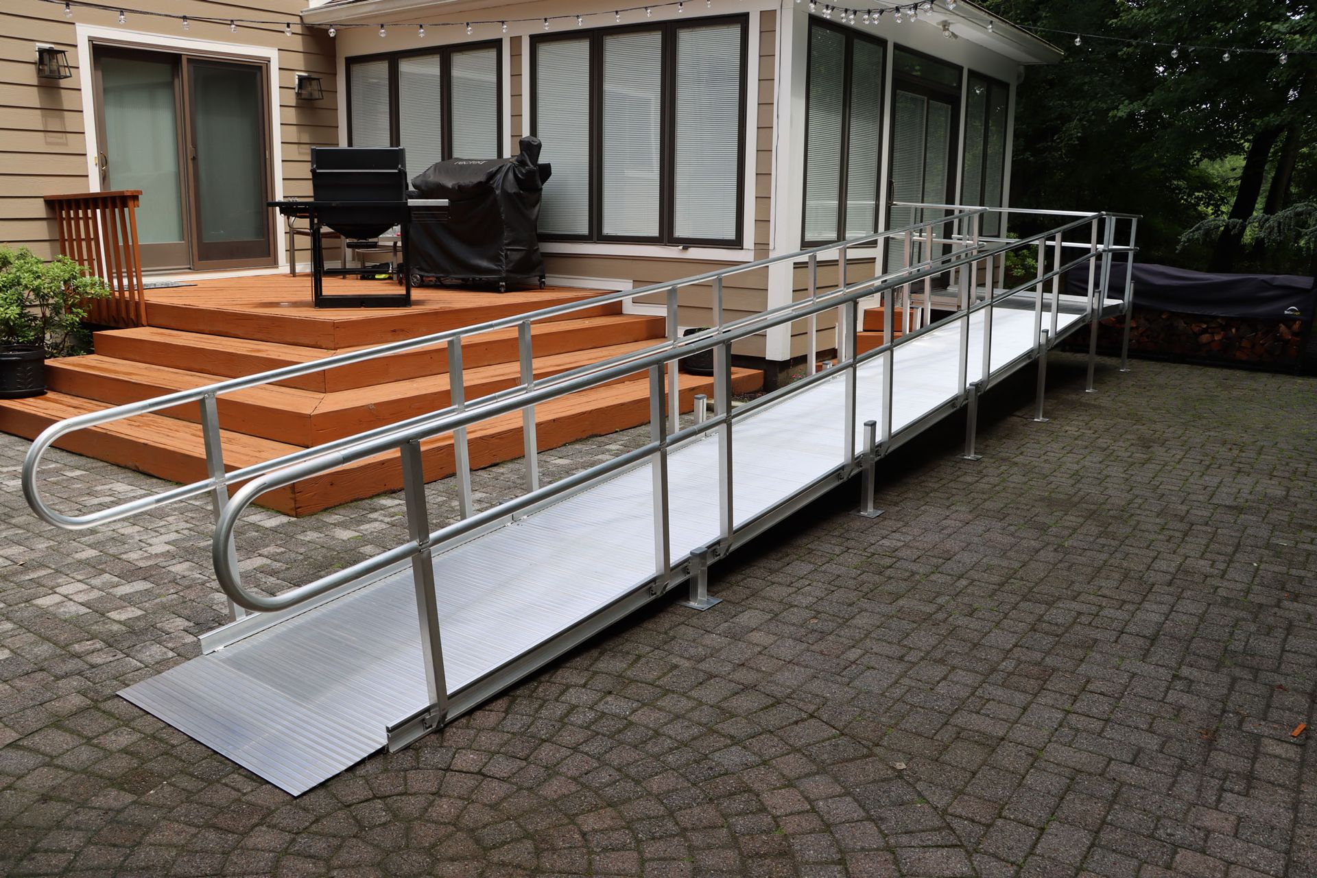 Aluminum ramp with handrails providing accessible entry to a wooden deck and enclosed patio.
