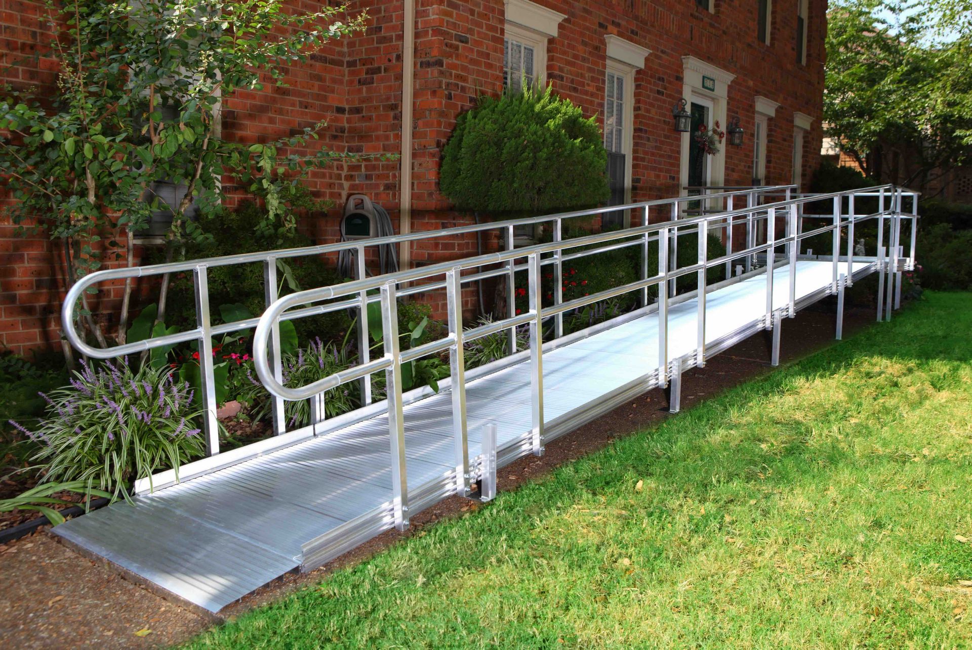 Metal accessibility ramp with handrails beside a brick building and lawn