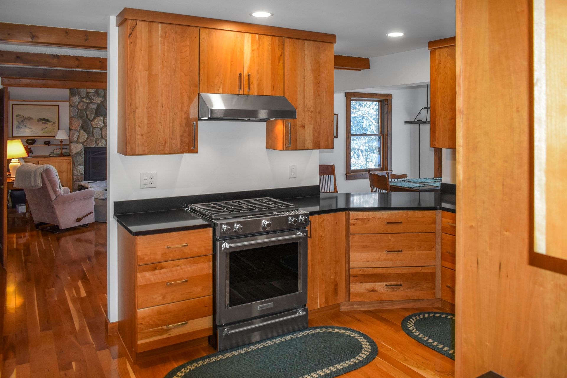 Kitchen with wooden cabinets, black countertops, stainless steel stove, and hardwood floors.