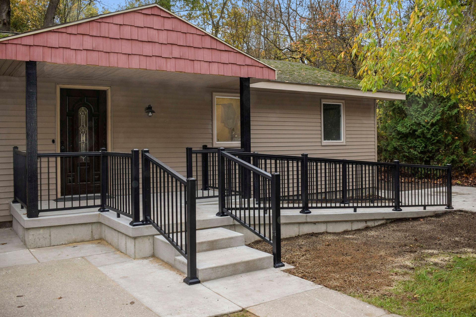 Ramp and steps leading to a house with a porch and red roof. Black handrails, tan siding.