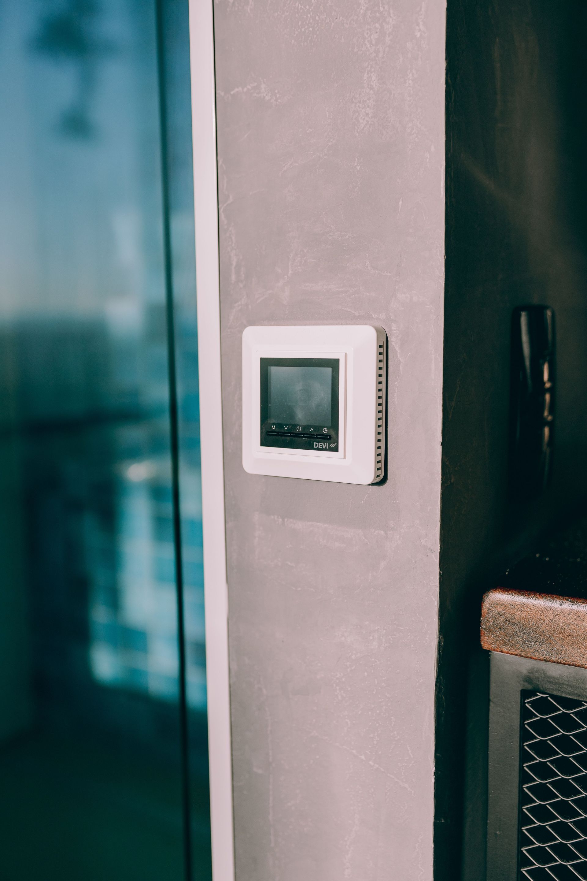 White wall thermostat mounted beside a dark door and teal-tinted glass panel