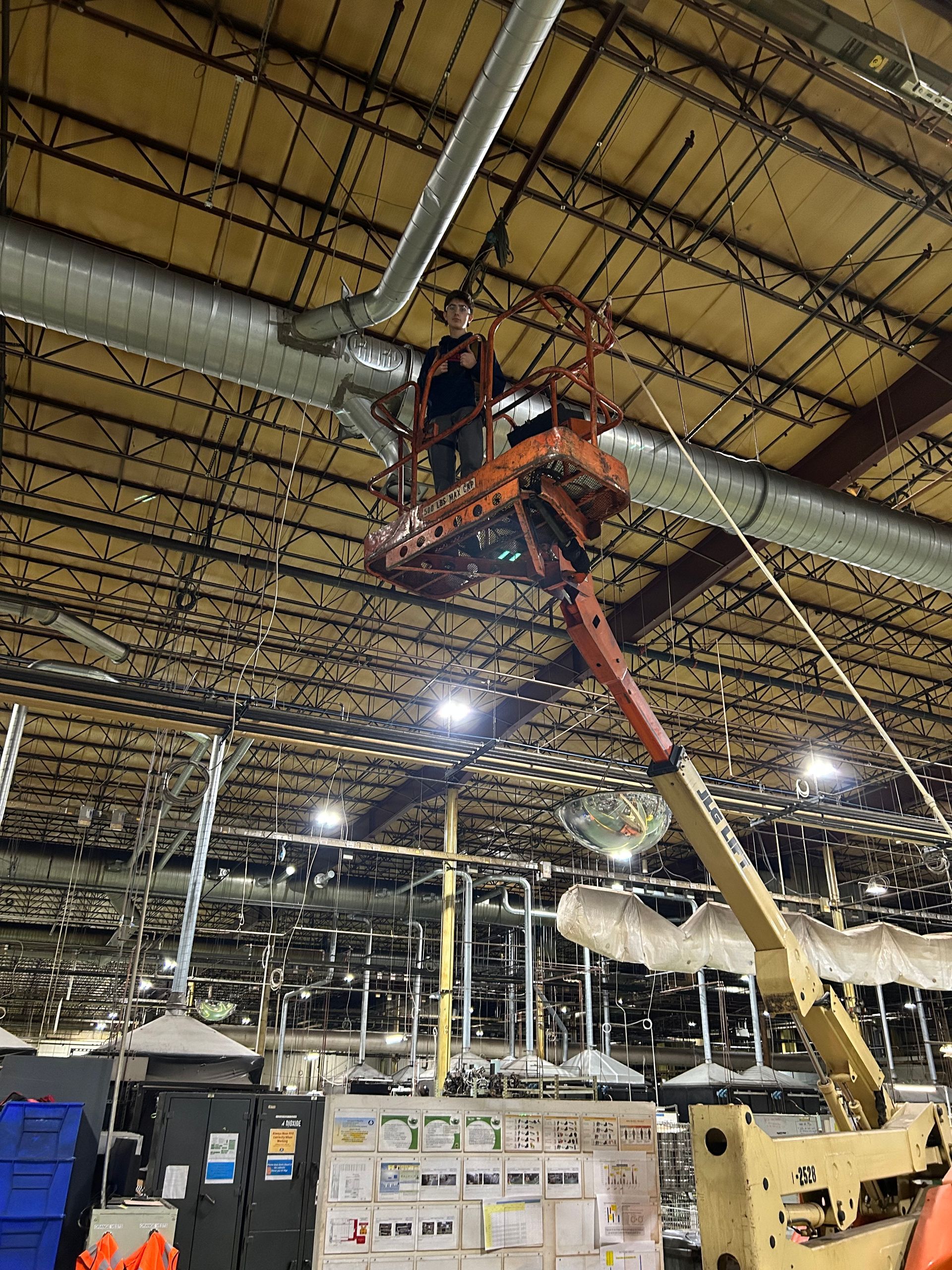 Person on a lift working on overhead ductwork in an industrial setting.