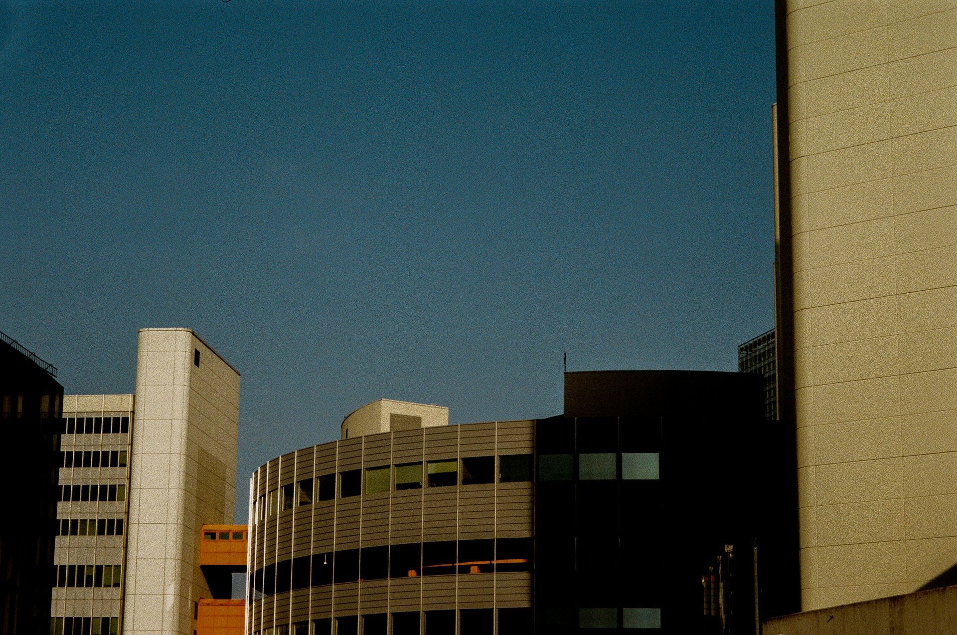 City buildings silhouetted against a blue sky, varied architecture with shades of tan and dark colors.