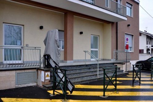 Esterno di un edificio con gradini e un oggetto coperto vicino all'ingresso, linee gialle per l'attraversamento pedonale.