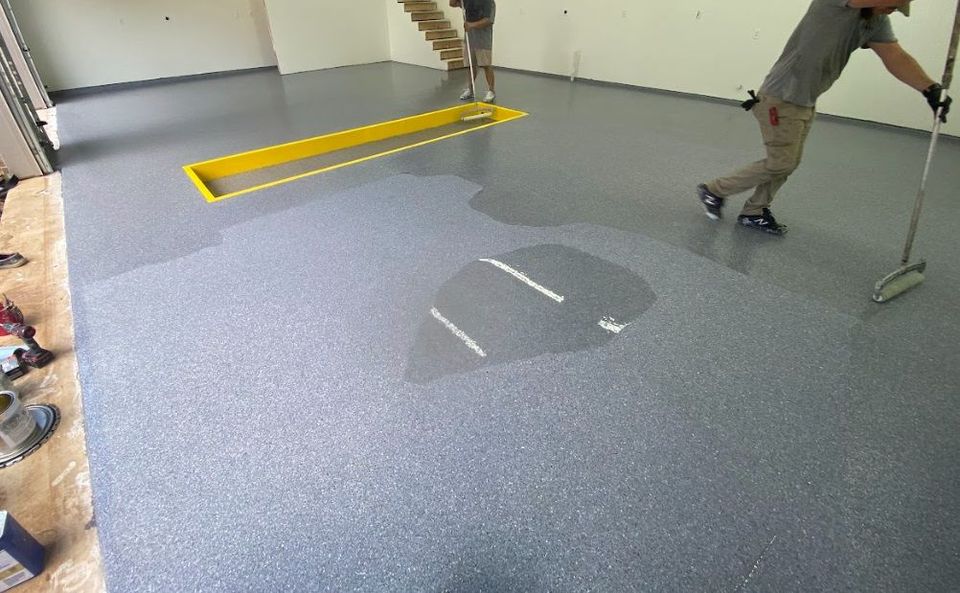 A man is painting a garage floor with a roller.