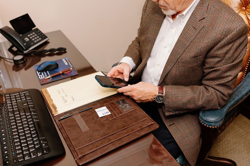 Person using a smartphone at a desk with a laptop, keyboard, and office phone.