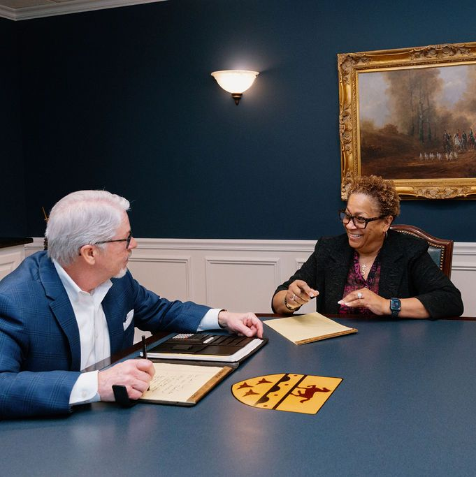 Two people in a conference room reviewing papers across a table.