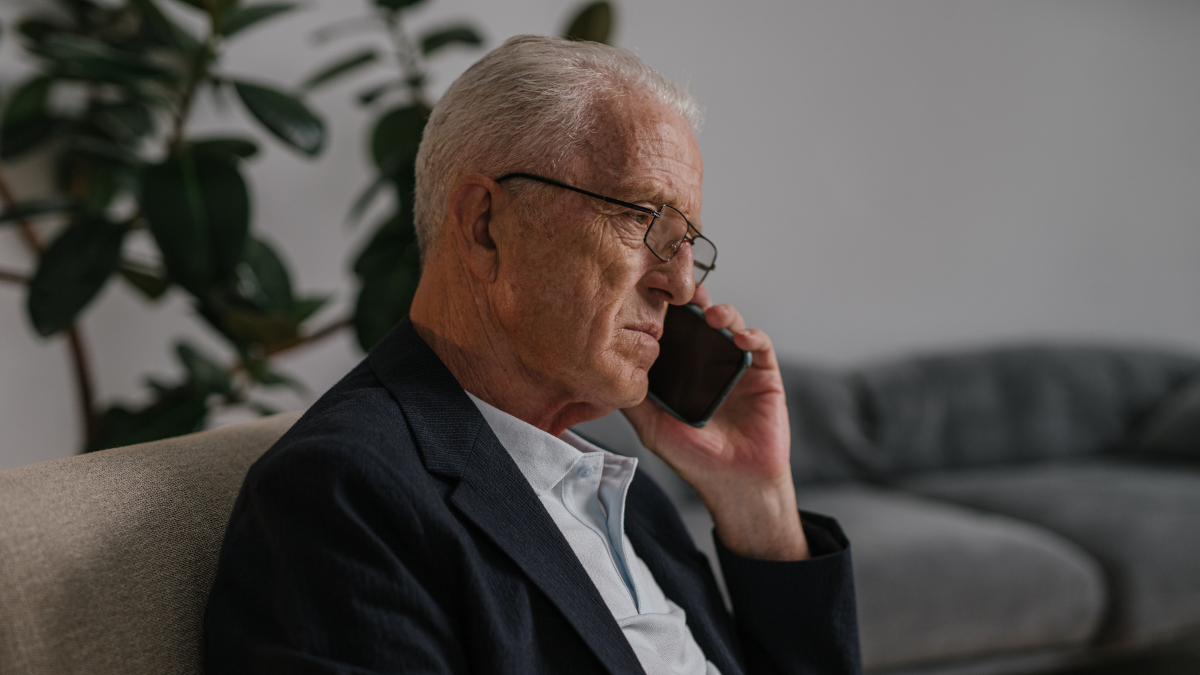 Man in a dark suit talking on a phone while seated on a couch in a modern living room