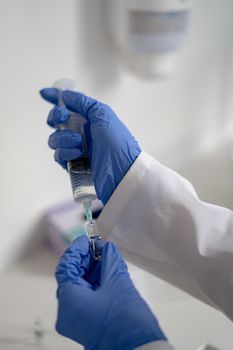 Gloved hands of a doctor preparing a syringe for an injection
