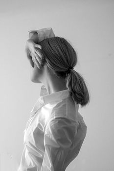 Woman in profile with hair tied back against a neutral wall