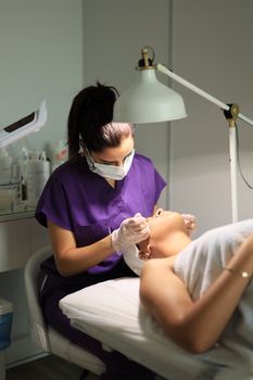 Dermatologist examining redness on a woman's cheeks under a magnifying lamp