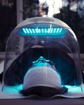 Woman lying under a blue LED light therapy panel in a clinic