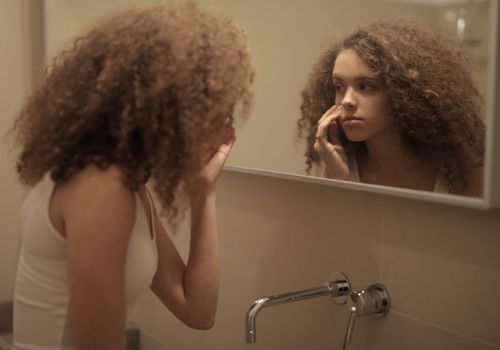 Woman touching the angle of her jaw while looking in a mirror
