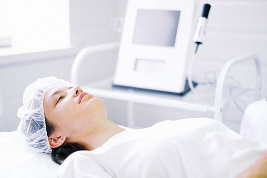 Woman resting on a treatment bed while a device treatment is performed on her face