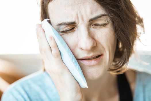 Woman holding a cold compress to her cheek at home