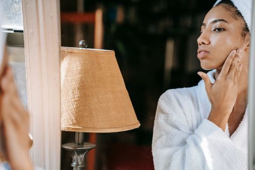 Woman with hydrated, glowing skin touching her cheek in window light