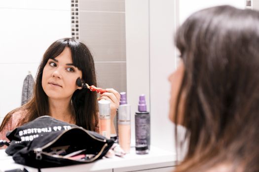 Woman applying light foundation with a makeup sponge at a bathroom mirror