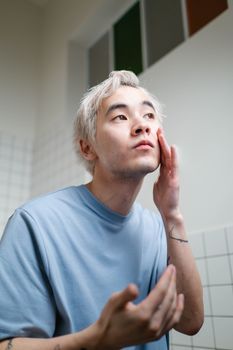 Young man looking closely at his skin in a bathroom mirror