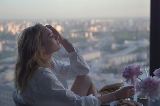 Woman relaxing by a sunlit window overlooking a city skyline