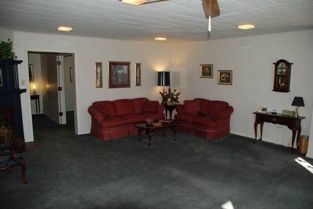 Spacious living room with red sofas, dark carpet, wall art, and small tables.