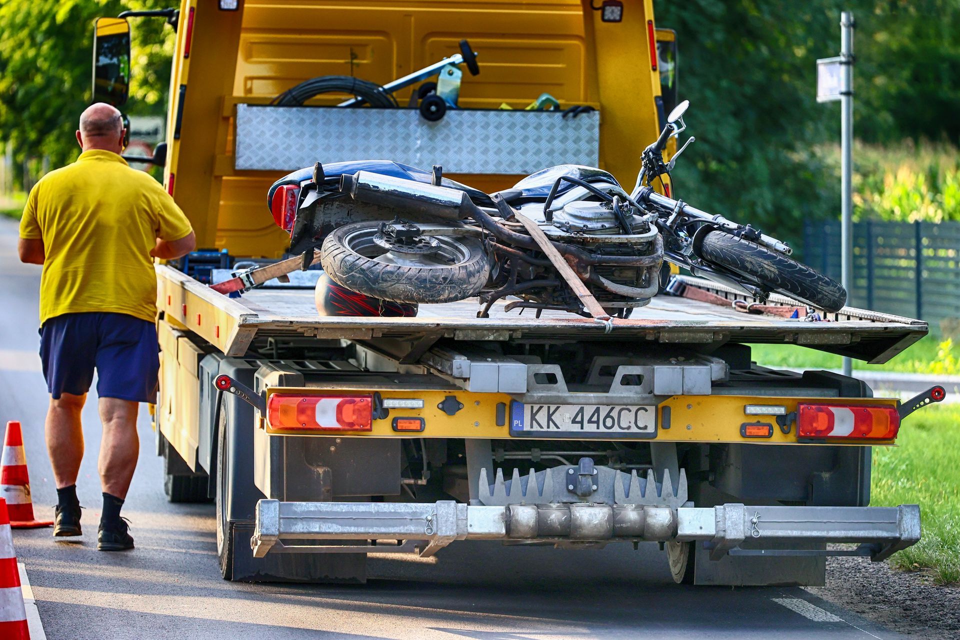 Tow truck loading a crushed motorcycle on a road, with a worker in a yellow shirt nearby