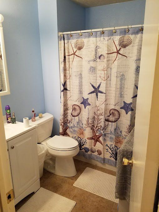 Small bathroom with a white toilet, sink cabinet, and blue starfish shower curtain.