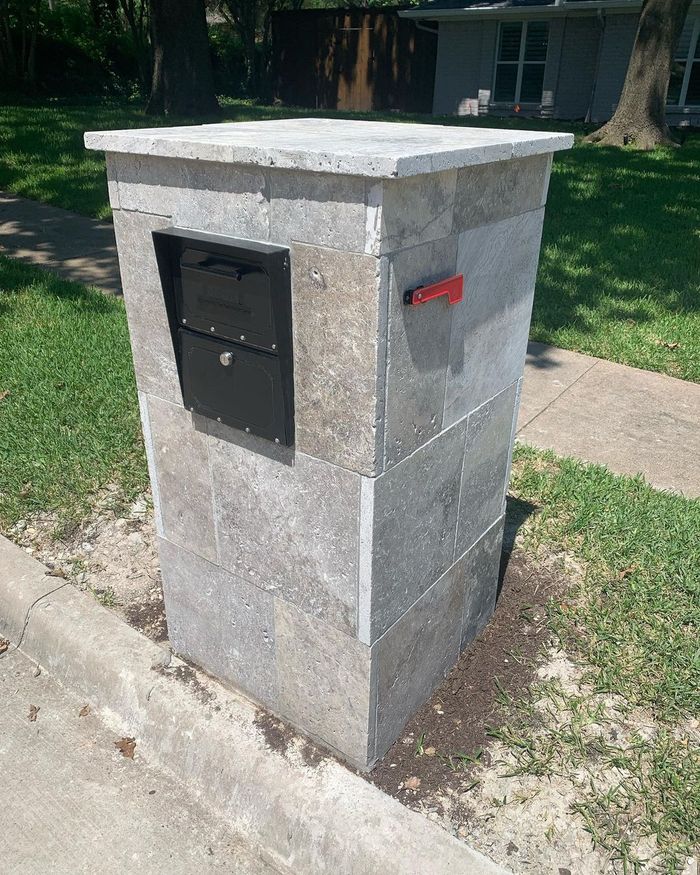 Stone pillar mailbox beside a sidewalk in a grassy residential yard
