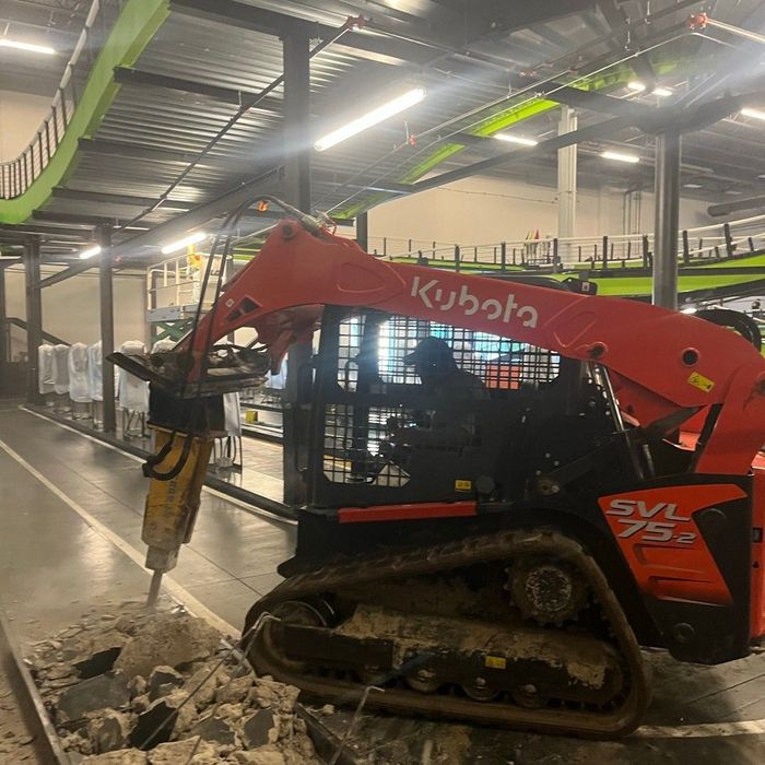 Red Kubota excavator breaking concrete indoors at a construction site