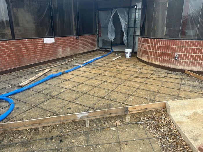 Construction site with brick retaining walls, rebar mesh, blue hose, and a doorway in the background