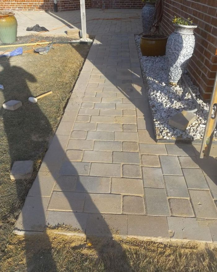 Front walkway with gray pavers, brick wall, potted plants, and long shadows in sunlight