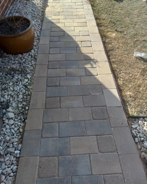 Stone paver walkway between gravel beds and a patch of grass in a yard