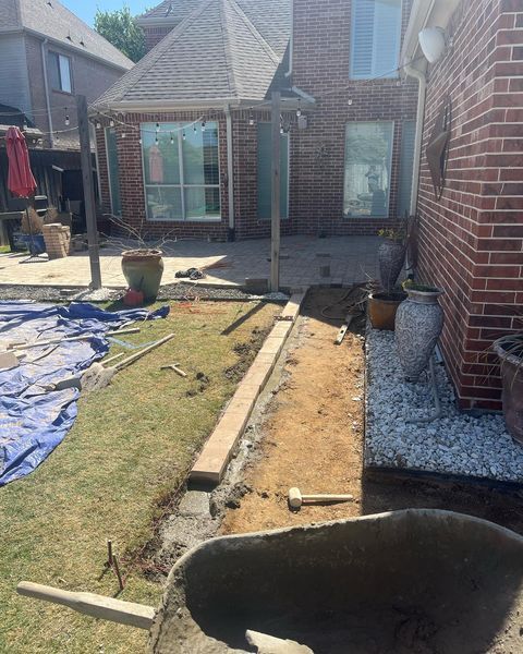 Backyard patio under construction with dirt trench, tools, and a brick house wall