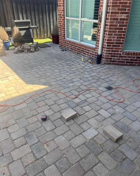 Brick patio with loose pavers and a black cord near a brick house wall