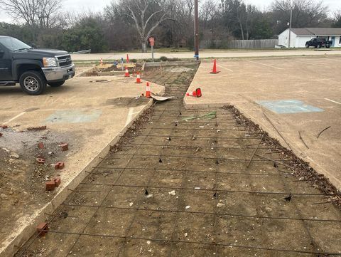 Construction cones marking a broken sidewalk path beside a parking lot and road